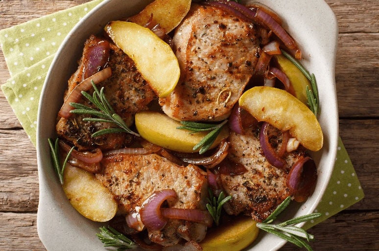 Pan with seasoned pork chops topped with apple slices and caramelized onions.