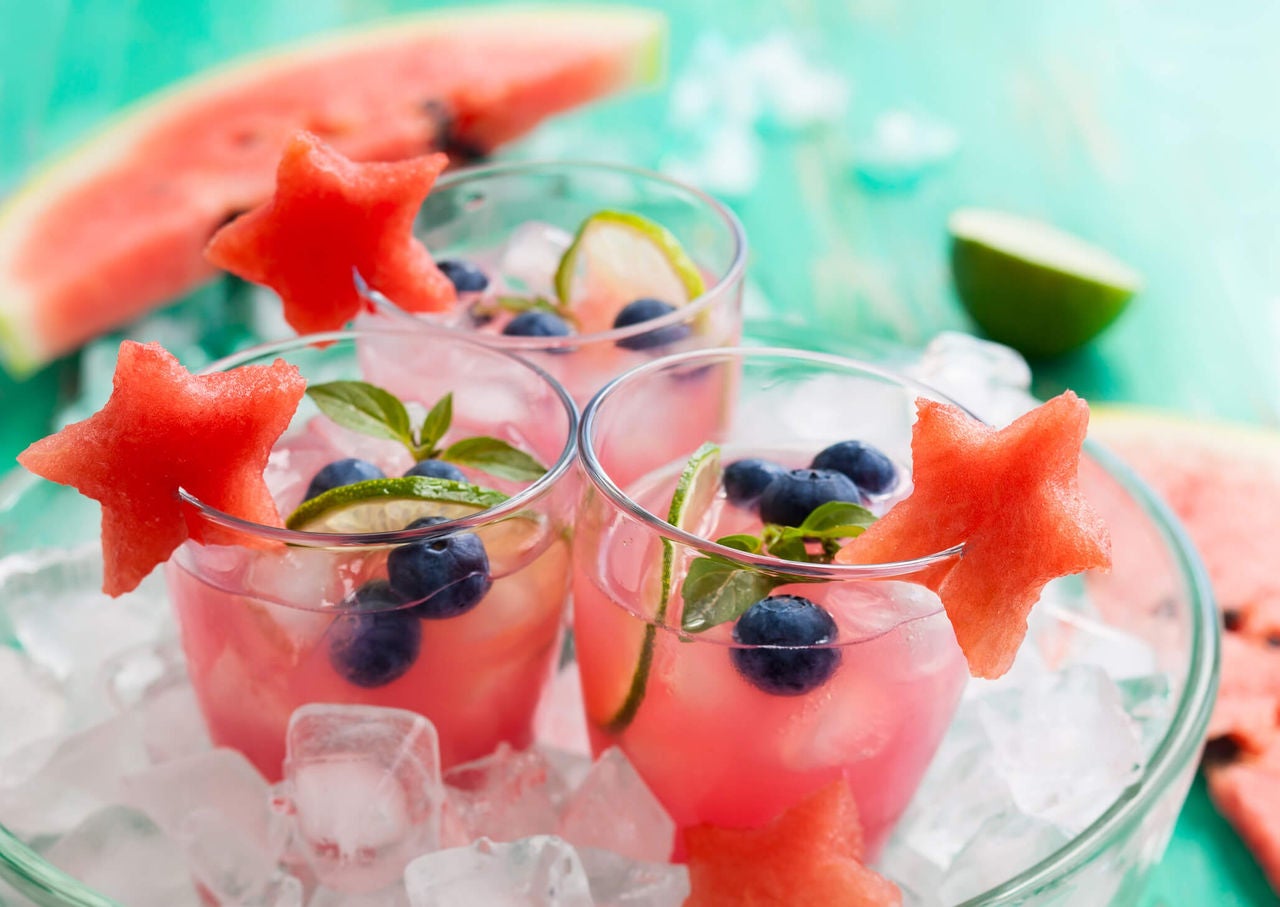 Glasses with pink drinks with blueberries, lime slices and star shaped watermelon garnish.