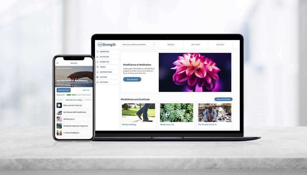 Laptop and smartphone displaying a mindfulness and meditation website with flower image, articles, and navigation menu on a light background.