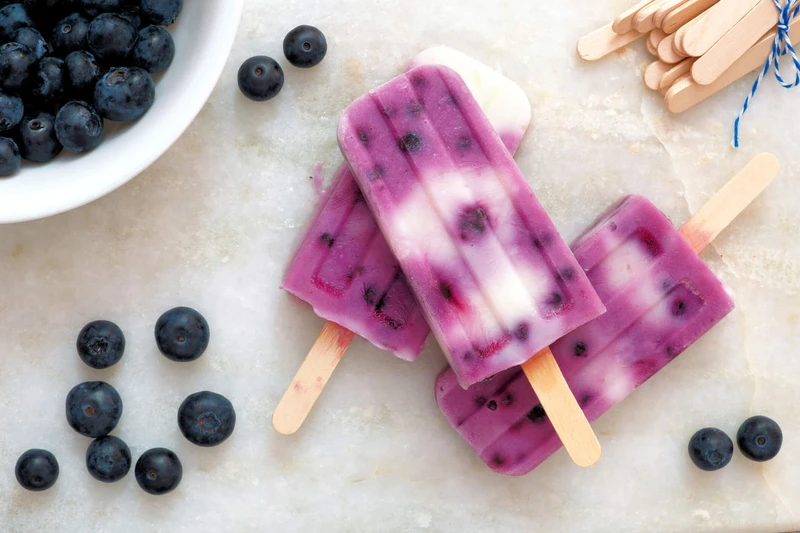 Blueberry and greek yogurt popsicles with blueberries on a marble surface.