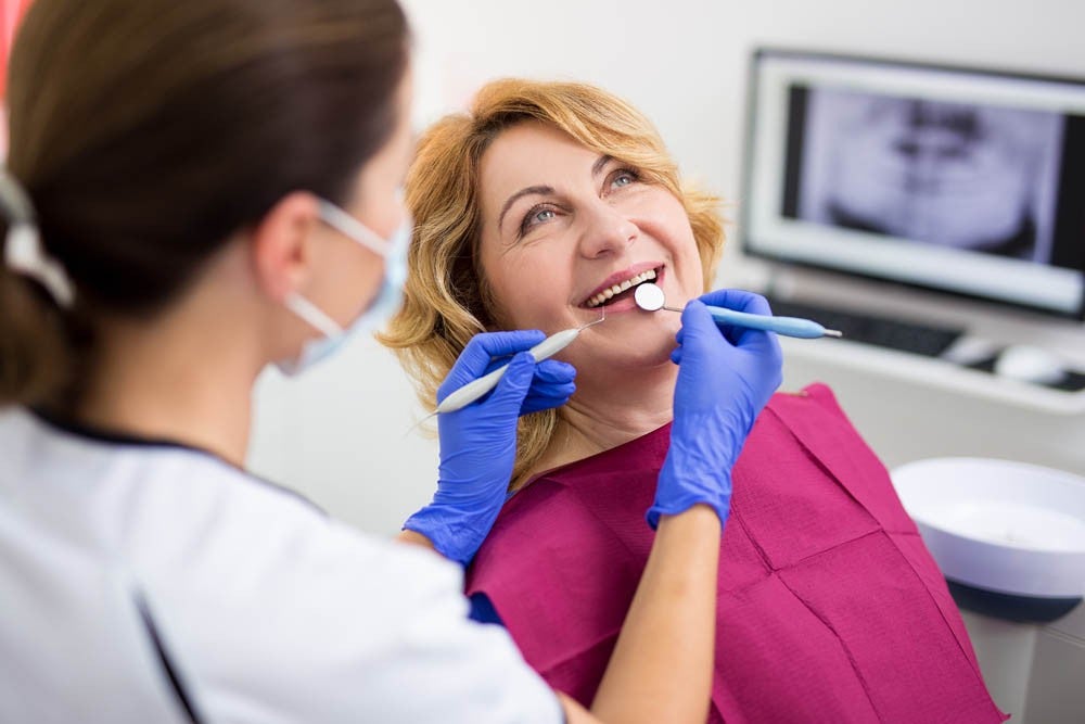 Mujer sonriente sentada en el sillón del dentista mientras la odontóloga realiza una revisión dental