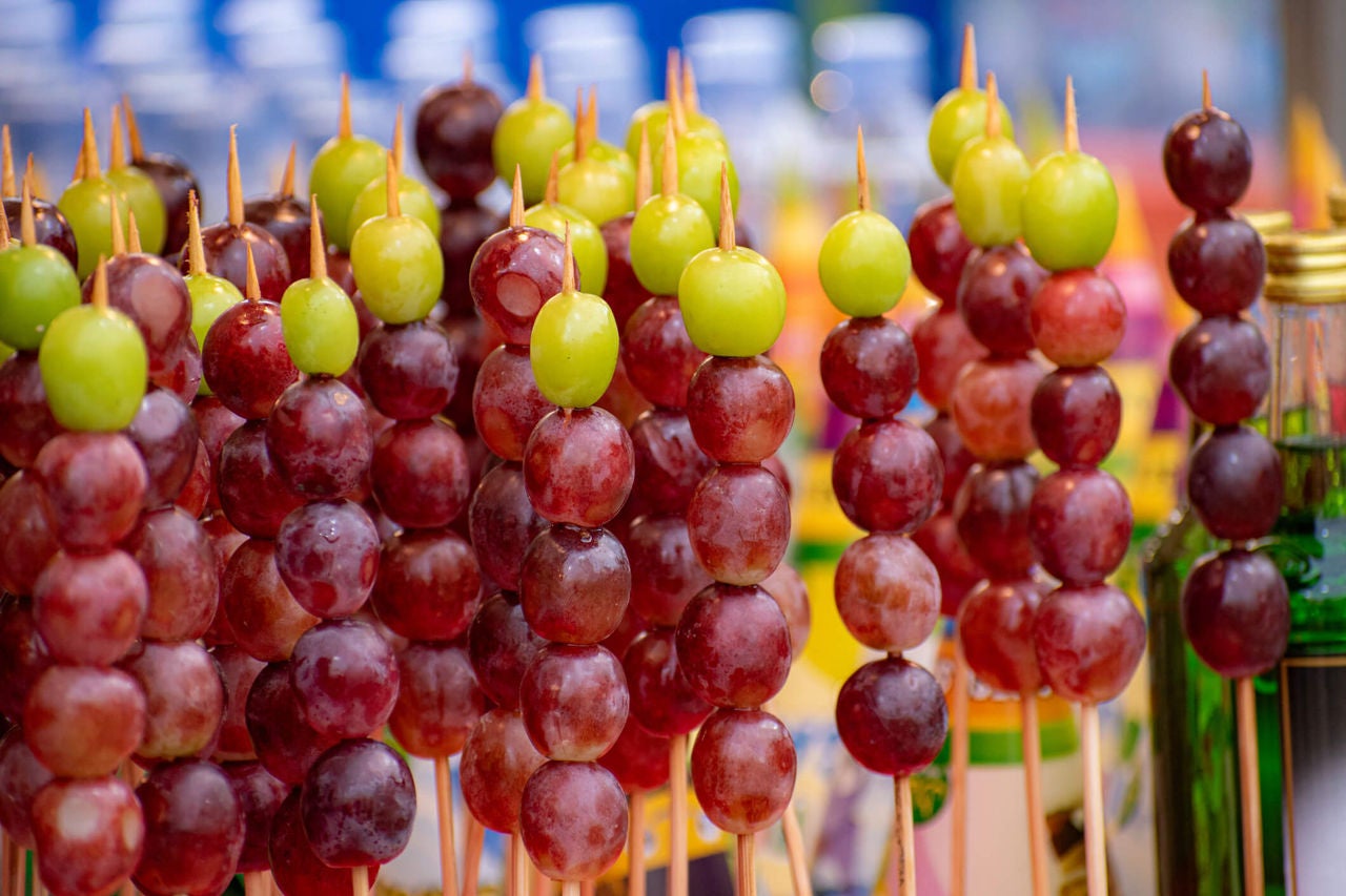 Large group of skewers with green and purple grapes on them.