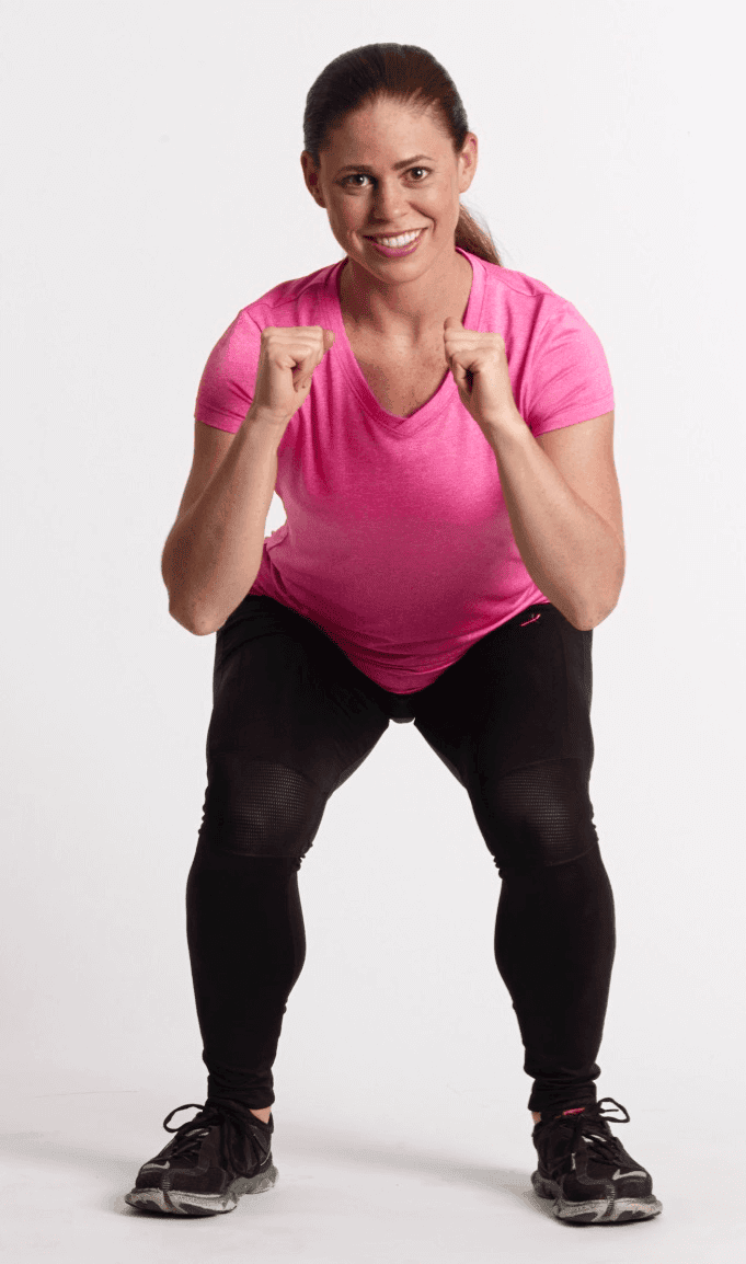 Mujer en posición de sentadilla parcial con los puños levantados, vistiendo camiseta rosa y leggings negros, sobre un fondo blanco.
