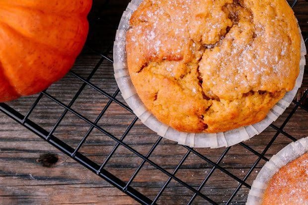 Pumpkin muffins on a rack with a pumpkin next to them.