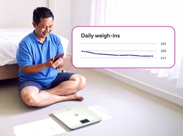 Man sitting on the floor with a scale looking at a mobile phone with inset saying "Daily weigh-ins" with a line chart