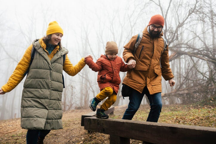 Parents holding hands of a small child while walking outdoors.