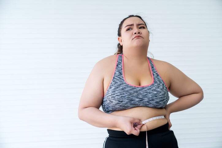 Woman measuring mid section with a tape measure while wearing athletic clothing.