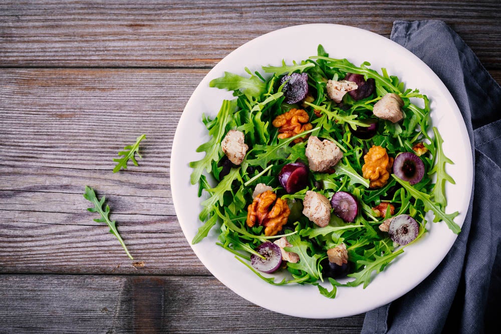 green salad bowl with arugula, walnuts, goat cheese, red onion and grapes on wooden background