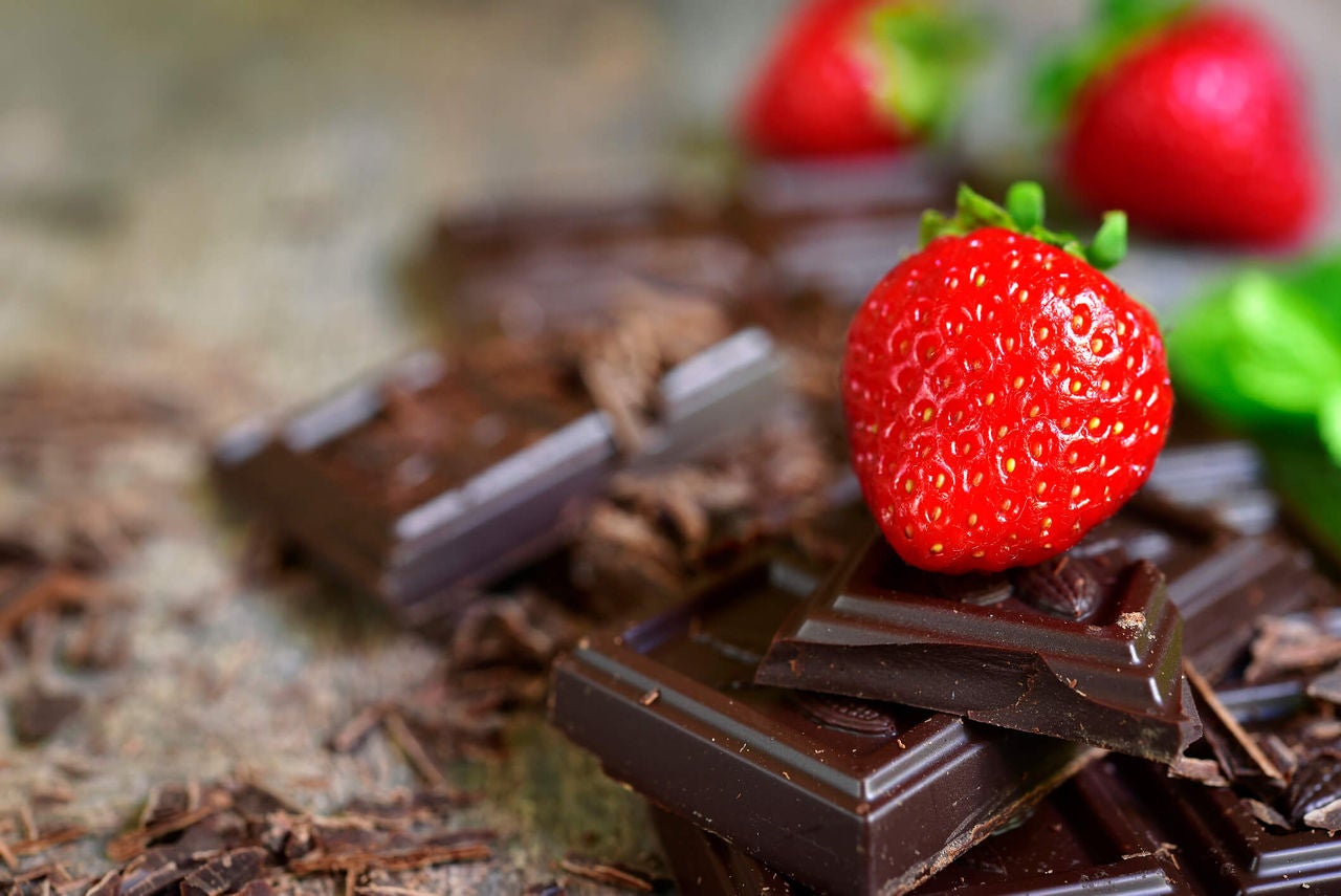 Pieces of a dark chocolate bar and a few strawberries on a wooden surface.