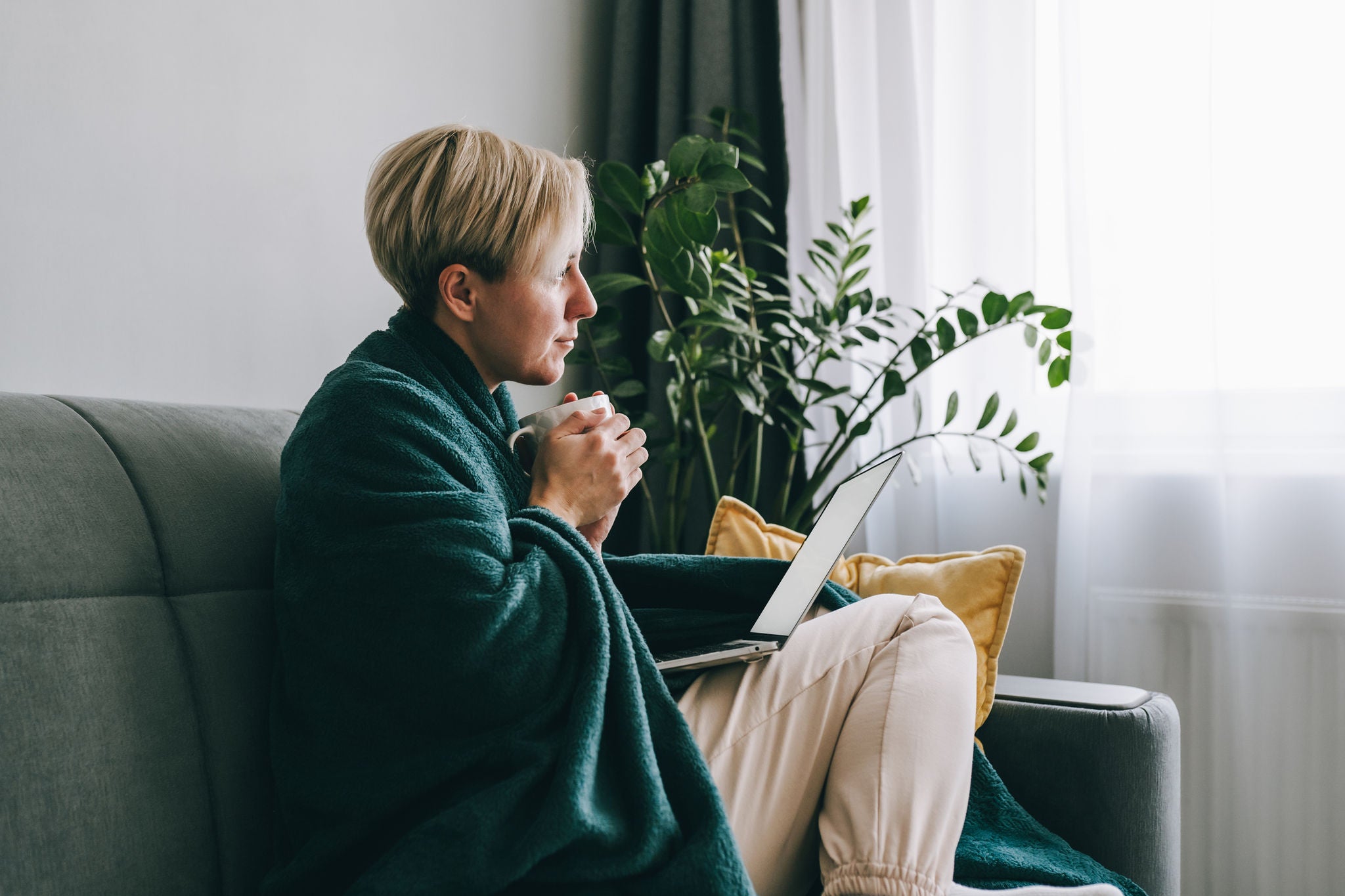 A woman drinking tea and looking out of a window.