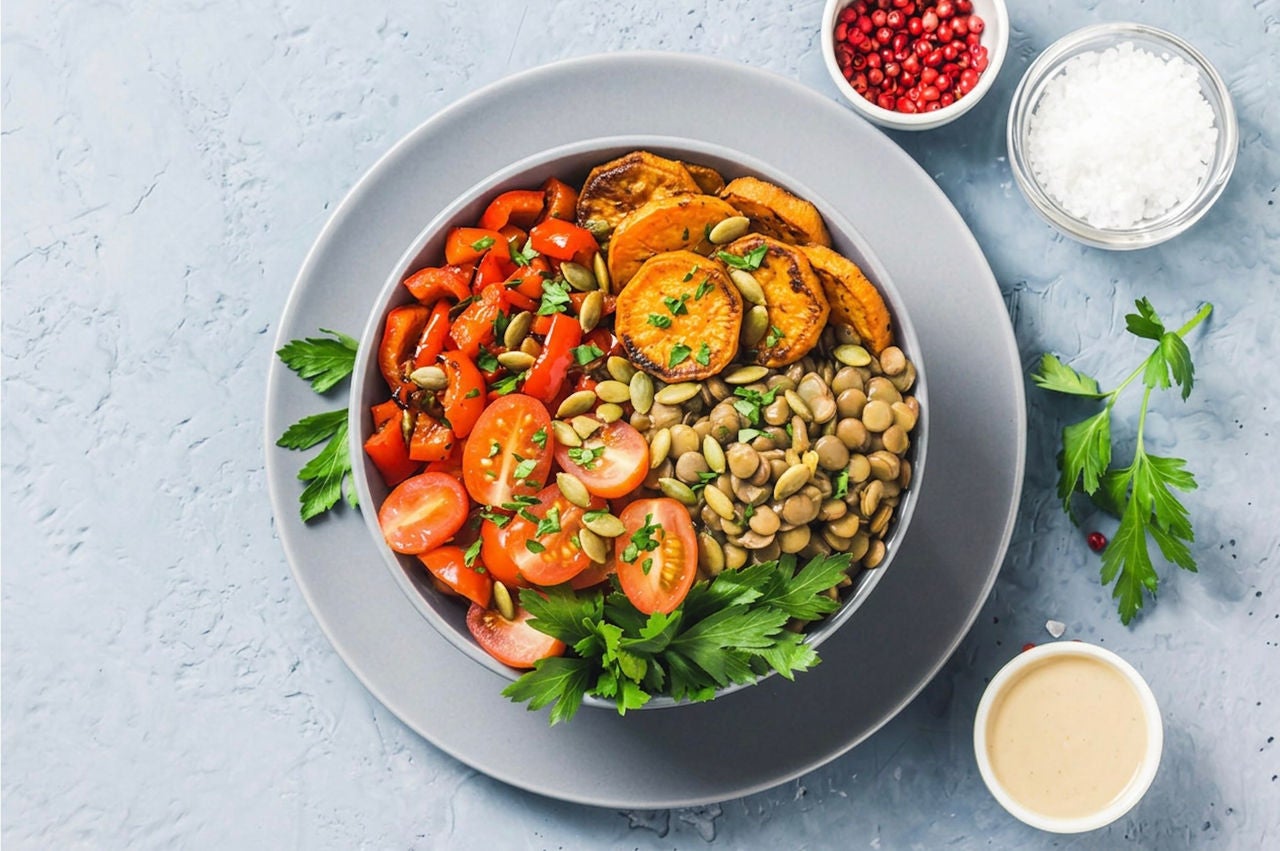 Overhead view of a large bowl with lentils, arugula, cherry tomatoes, red bell pepper pieces and sweet potato slices. 