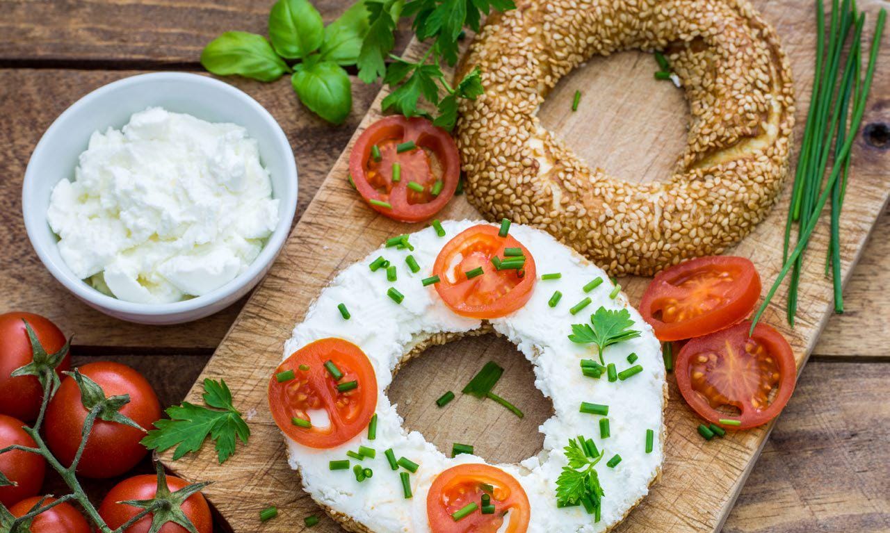Herbed cheese and tomato slices on half a bagel on a cutting board
