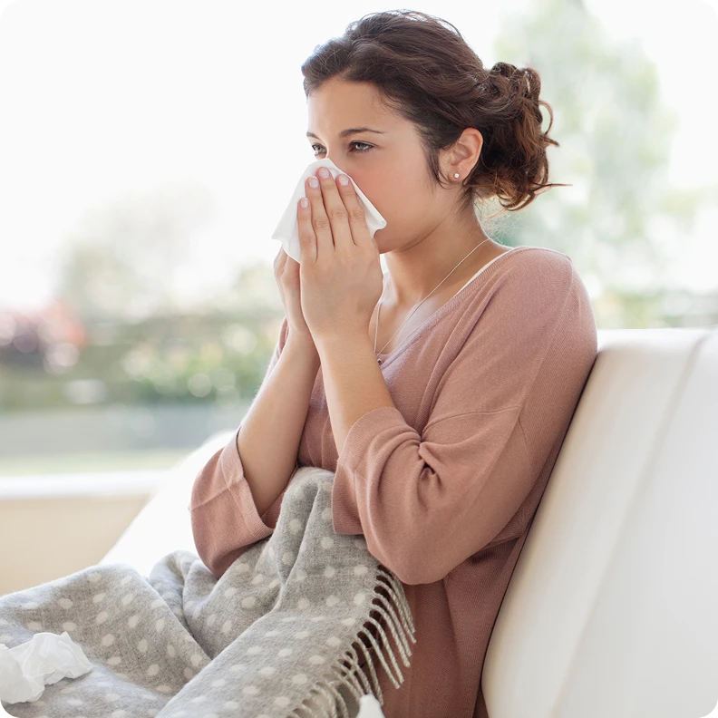 Woman sneezing into a tissue while sitting indoors during allergy season. 