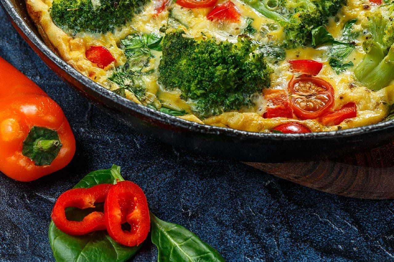 Cast iron pan with sunrise rainbow scramle in it with an orange pepper sitting next to it on a dark grey counter