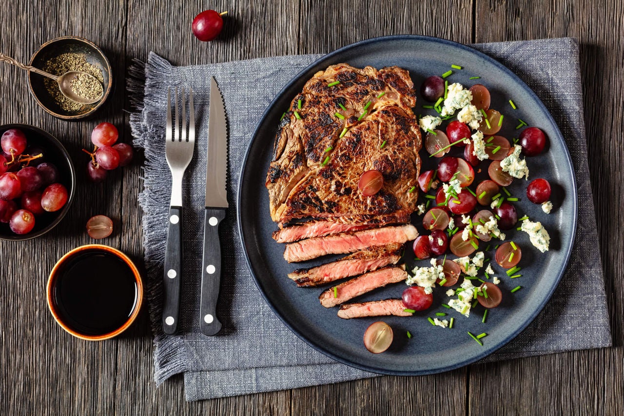 Sliced steak with a side of grapes and crumbled white cheese.