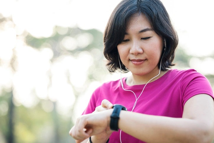 Woman outdoors wearing earphones and checking her fitness tracker.