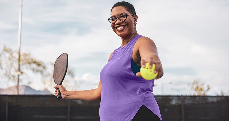 Woman holding pickleball and paddle