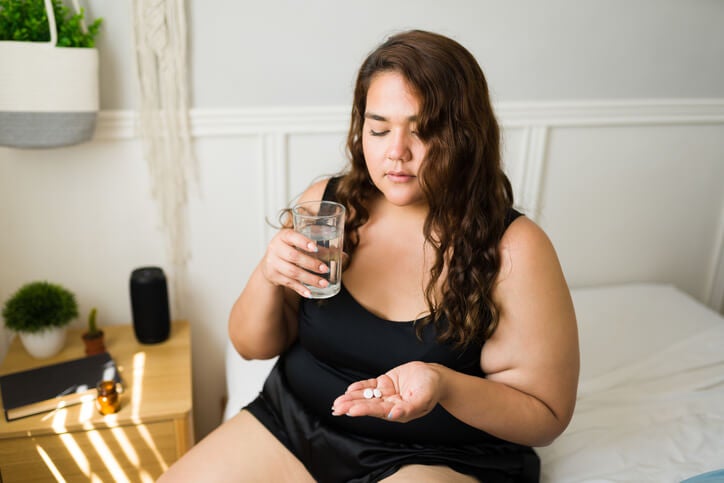 Woman sitting on bed with a glass of water and pills in her hand.