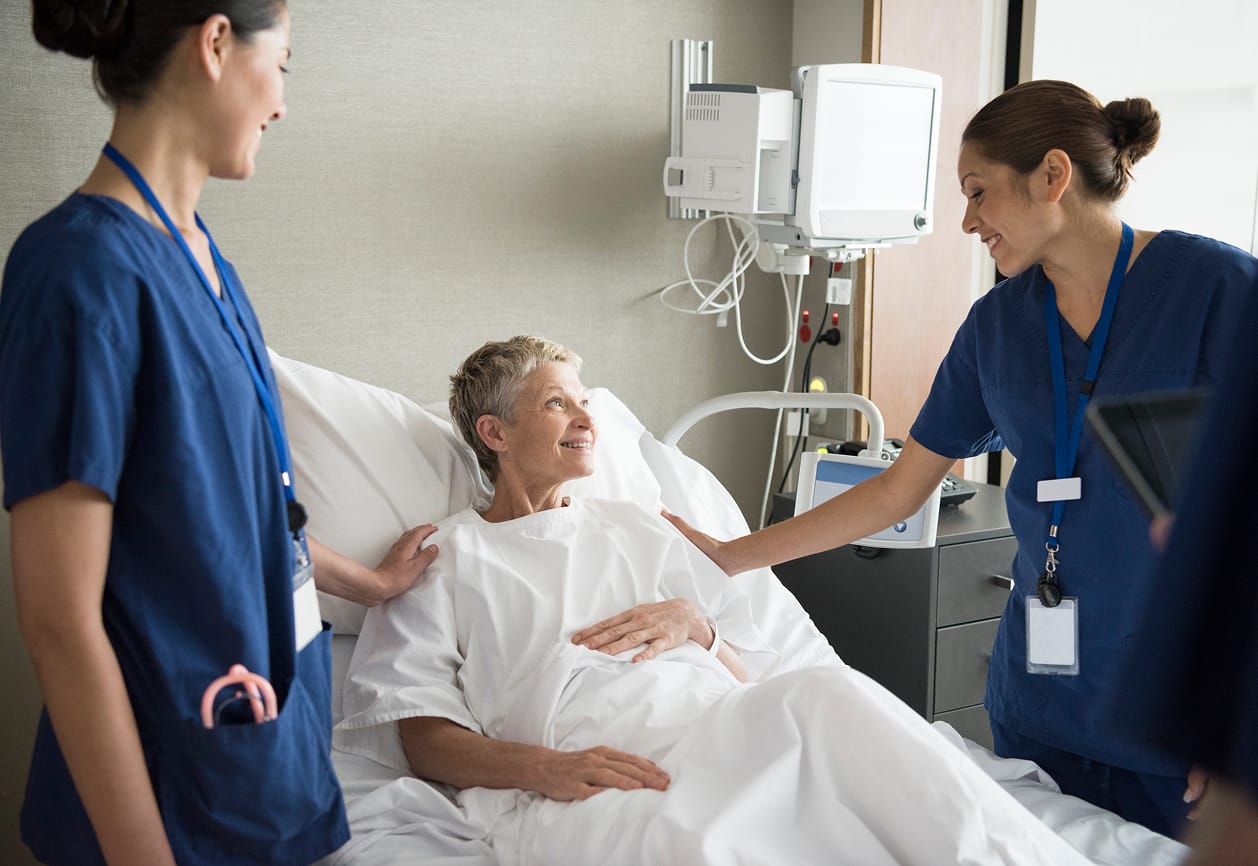 Nurses standing on each side of a patient in a hospital bed
