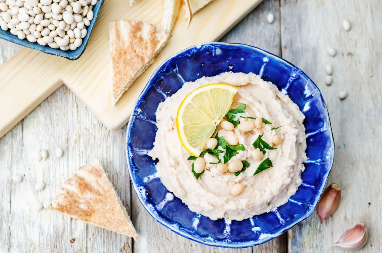 Blue bowl with creamy light dip and a lemon wedge next to pita triangles.