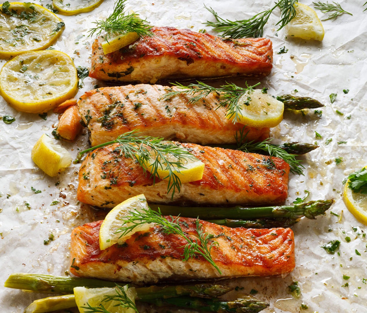 Salmon fillets with asparagus spears, lemon slices and dill on parchment paper.