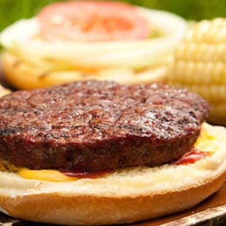 Hamburger on a bun with the top bun and corn on the cob in the background