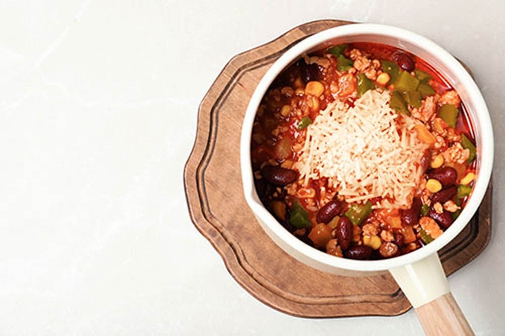 Saucepan with chili con carne, wooden board and space for text on light background, top view