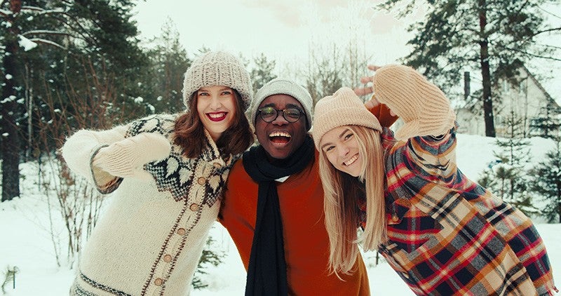  Three friends joyfully posing in a snowy landscape, wearing warm winter clothing and hats.