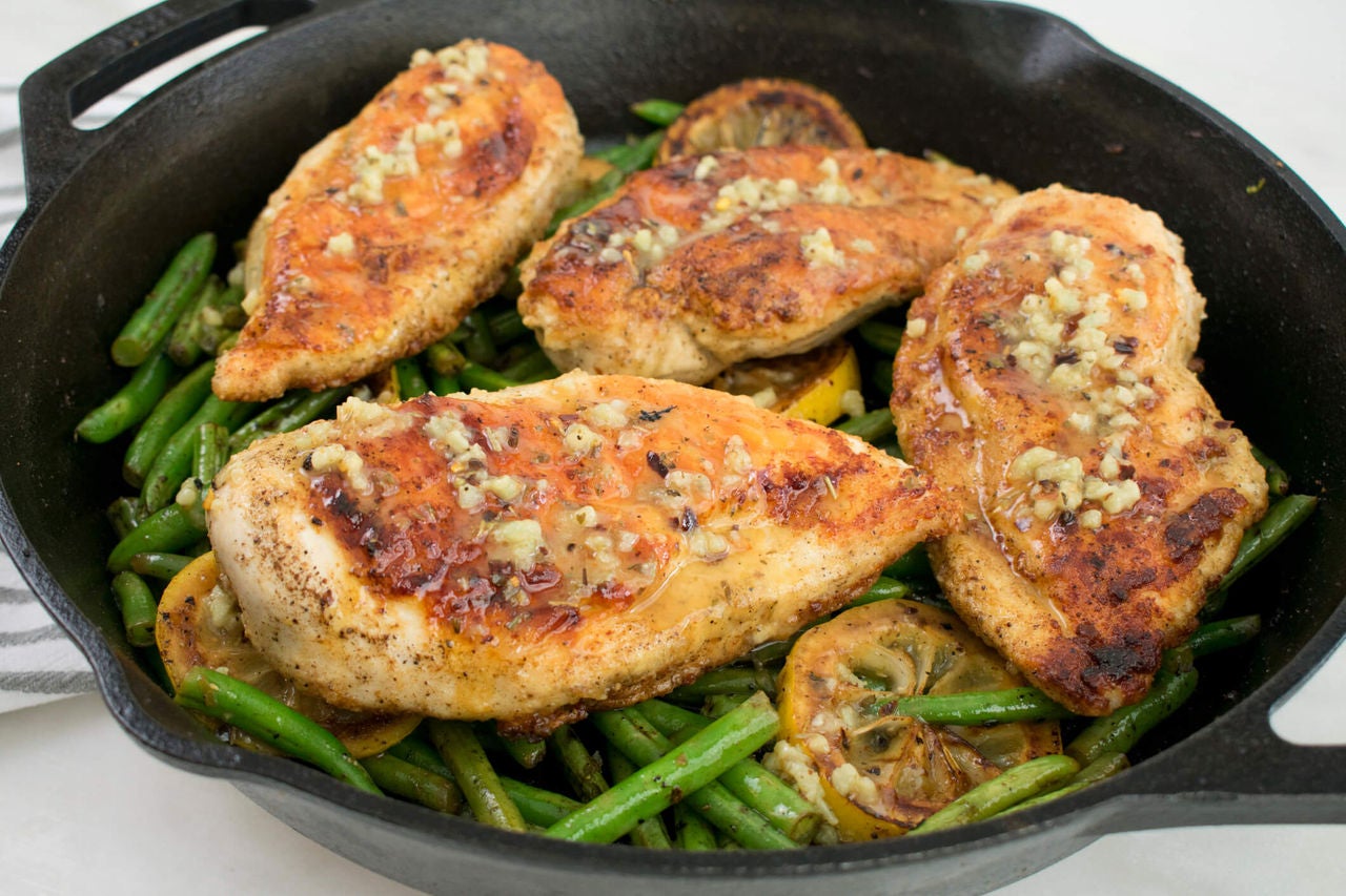 Skillet with seasoned chicken cutlets and green beans.