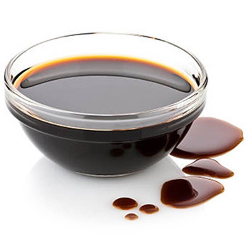 Cuenco de vidrio con salsa de soja derramada sobre una superficie blanca