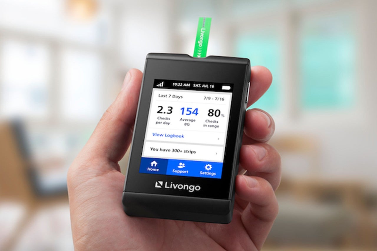 Hand holding a Livongo blood glucose meter displaying blood sugar readings.