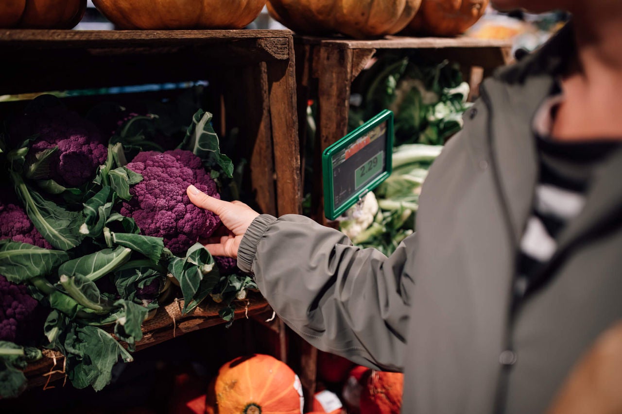 Person reaching for a purple cauliflower in a grocery store. 