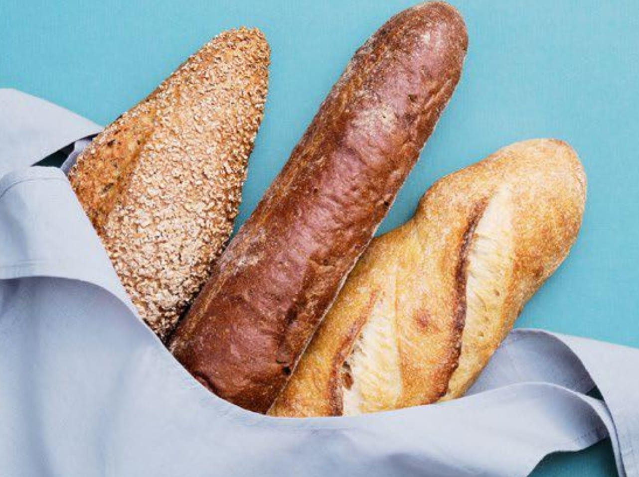 Three loaves of bread in a cloth bag on a light blue background.