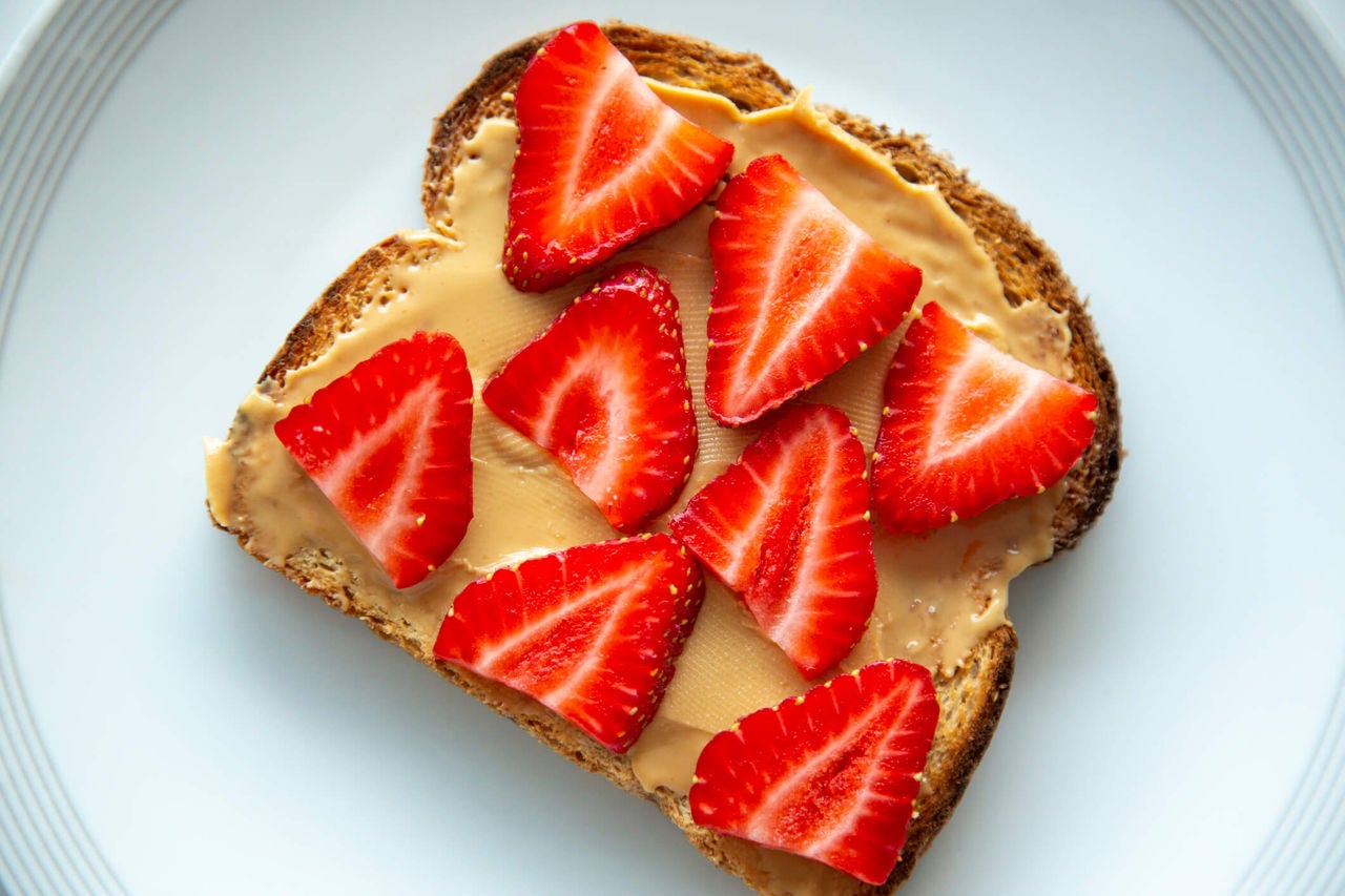 Slice of bread with peanut butter and sliced strawberries.
