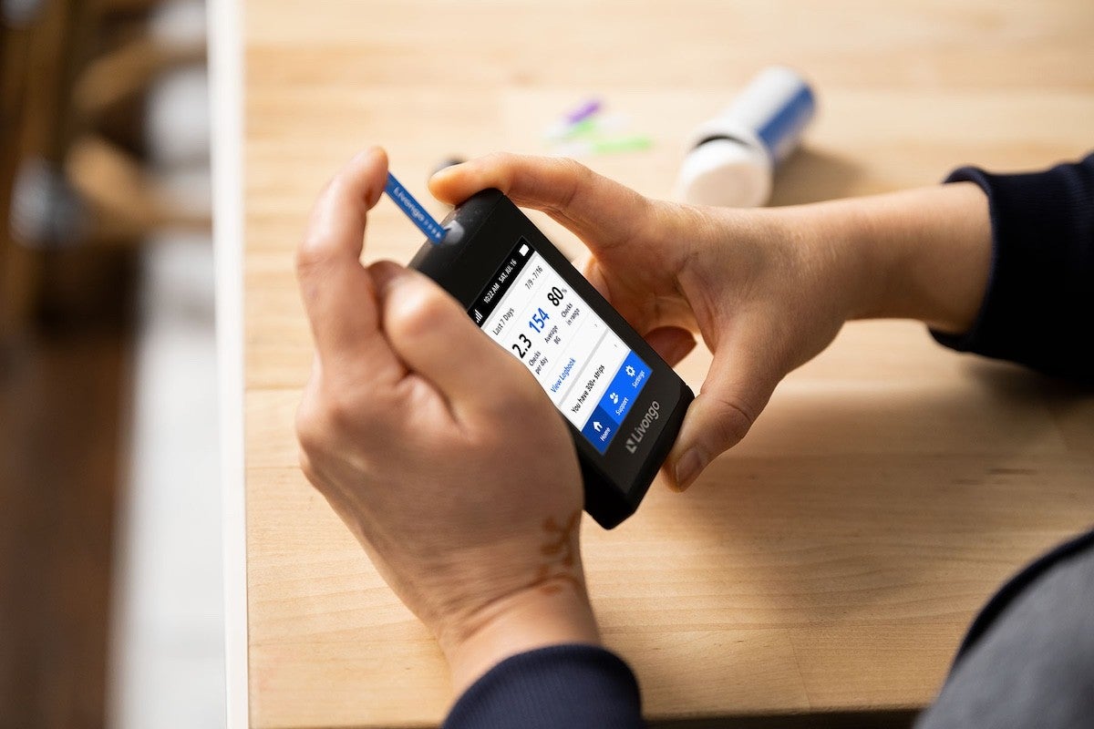 Person checking glucose levels with a glucometer at a wooden table.