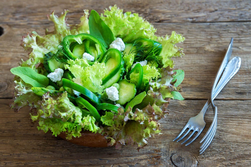 Organic mixed green vegetable salad with feta cheese in wooden bowl close up