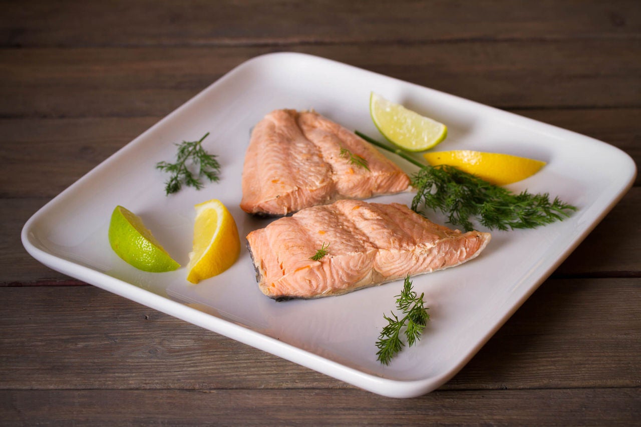 Two salmon fillets on a plate garnished with dill and lemons.