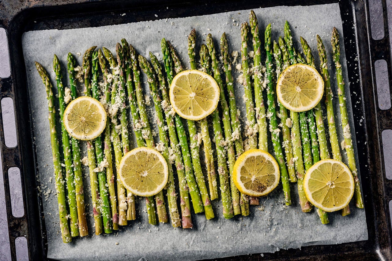 Asparagus spears with parmesan, seasoning and lemon slices on a pan.