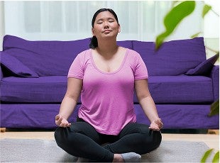 Woman sitting cross legged on the floor in front of a couch with eyes closed