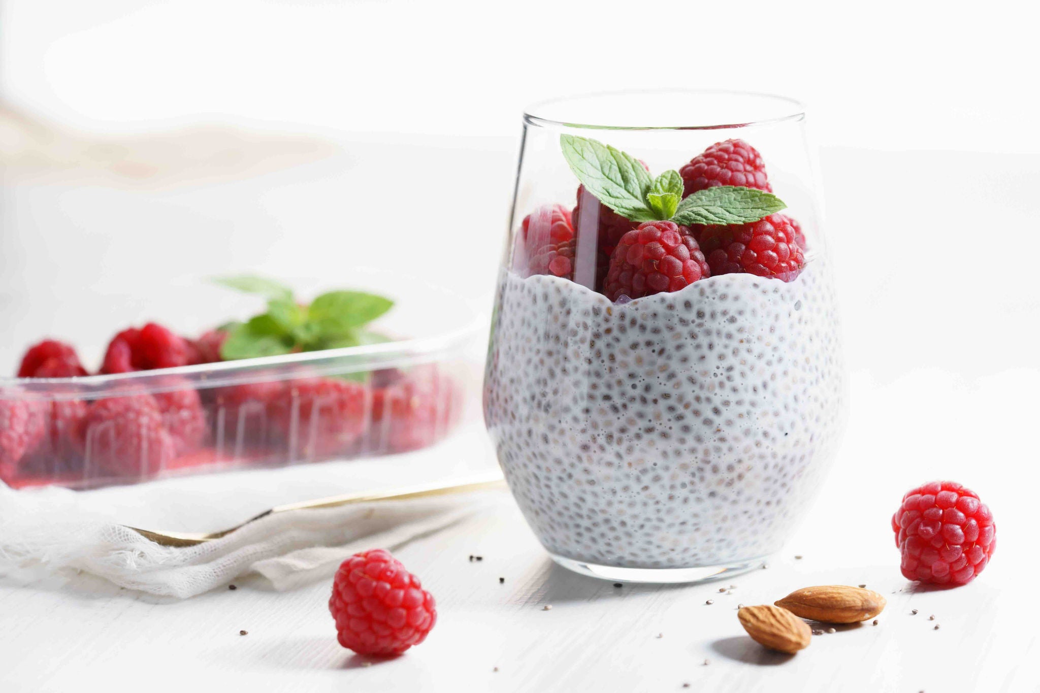 Cup with chia seed pudding topped with berries next to a carton of berries and two almonds.