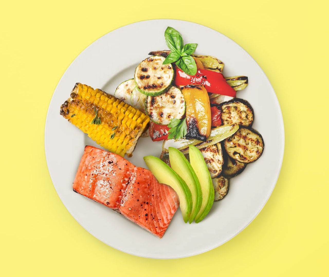 Plate of grilled salmon with corn, avocado, and mixed grilled vegetables.