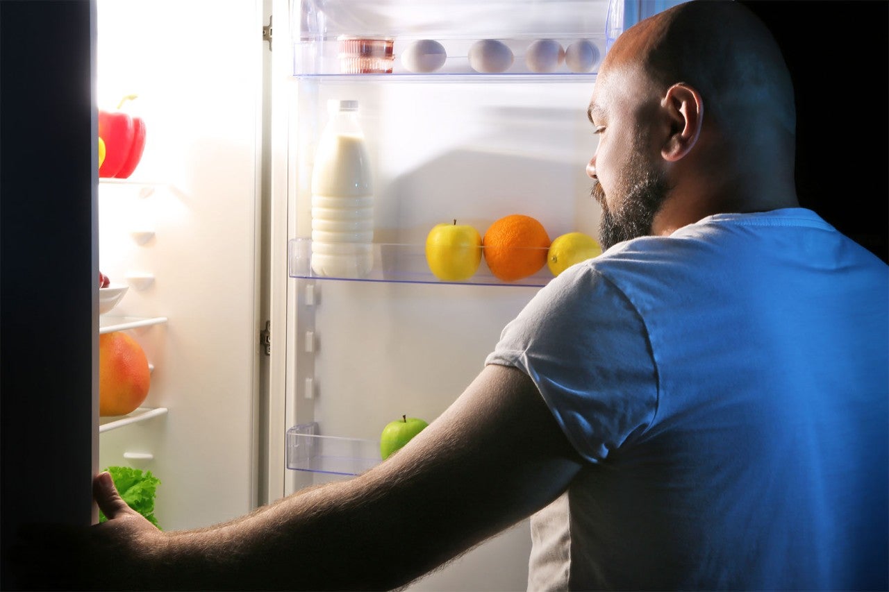 Man looking inside a refrigerator filled with fruits, milk, and eggs.