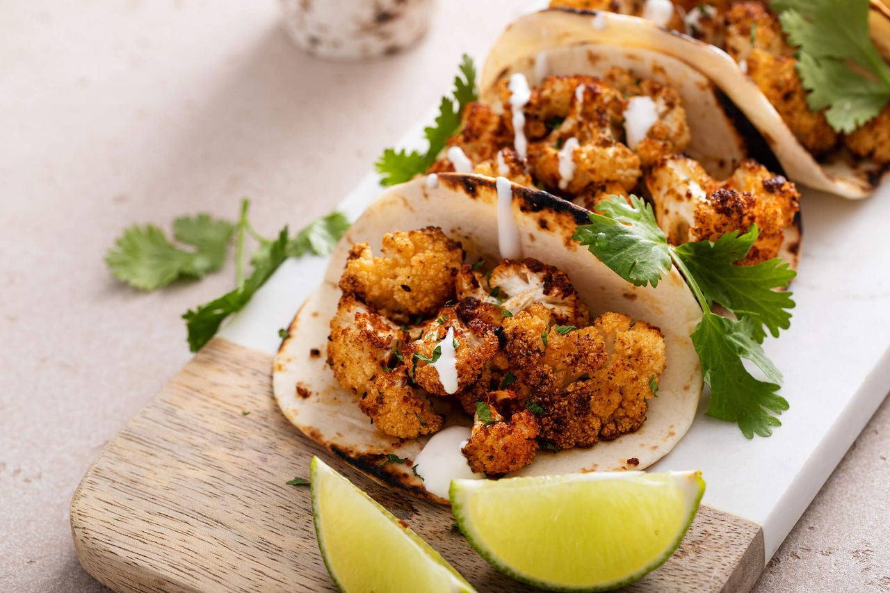 Tacos with cooked cauliflower florets and sauce with cilantro and lime wedges for garnish.