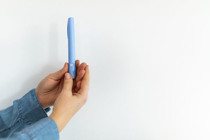 Set of hands holding an injection pen with both hands in front of a white background. 
