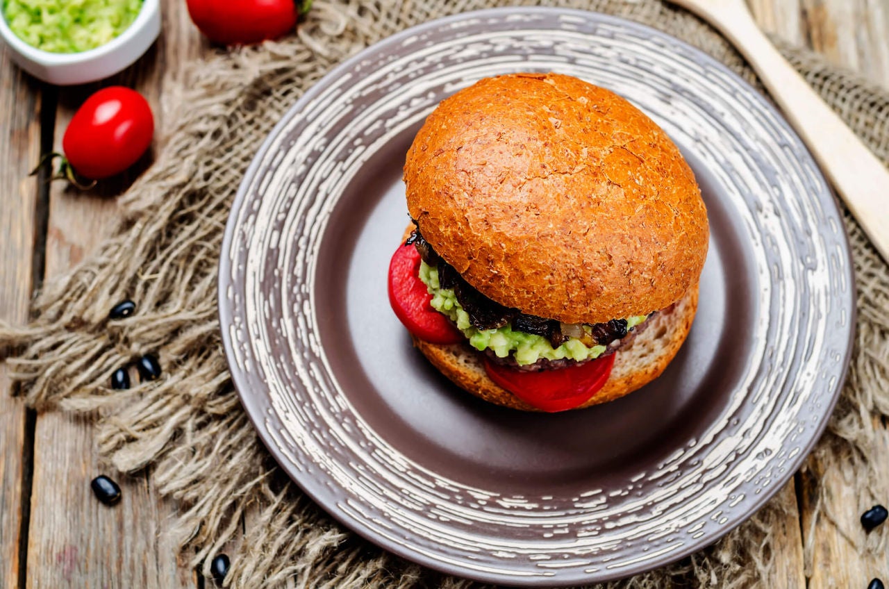 Burger with tomato slices and mashed avocado on a whole wheat bun.