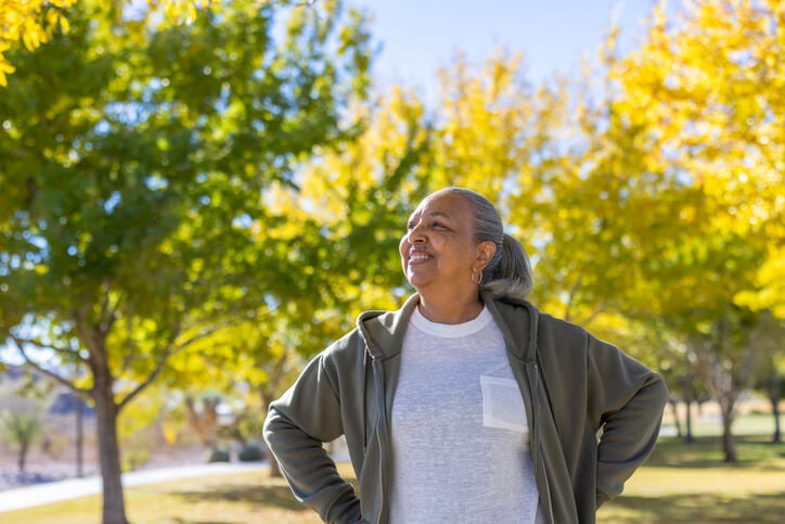 Older woman standing outside smiling confidently with her hands on her hips.