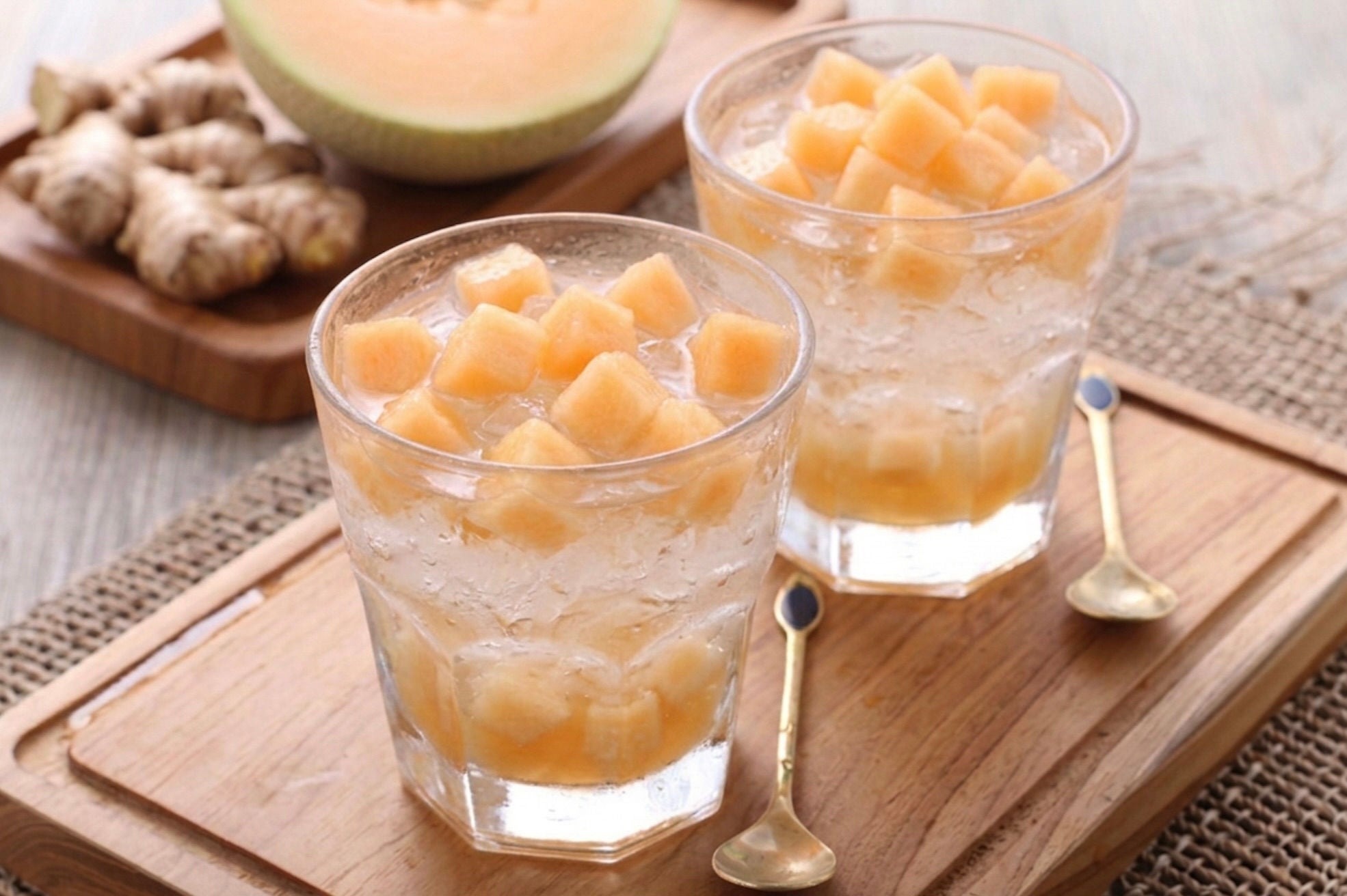 Glasses with water and melon cubes with a melon and ginger in the background.