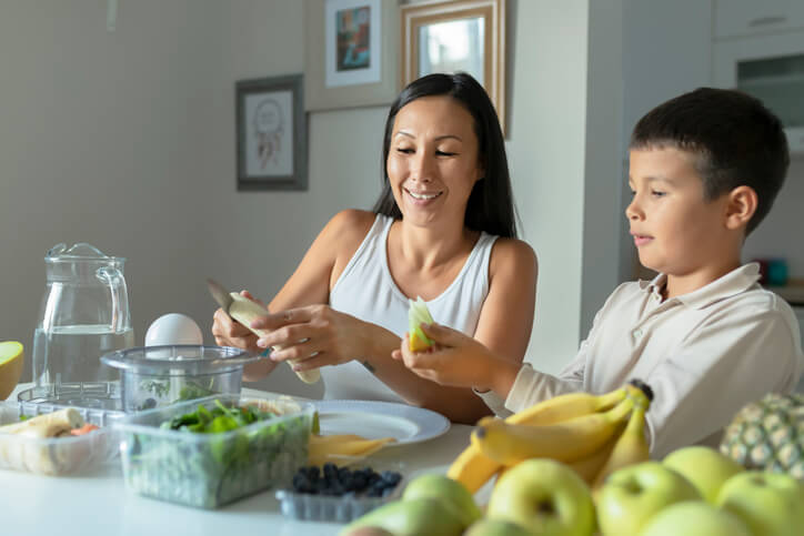 Mother and son preparing fruit and vegetables together at kitchen counter for school lunch prep