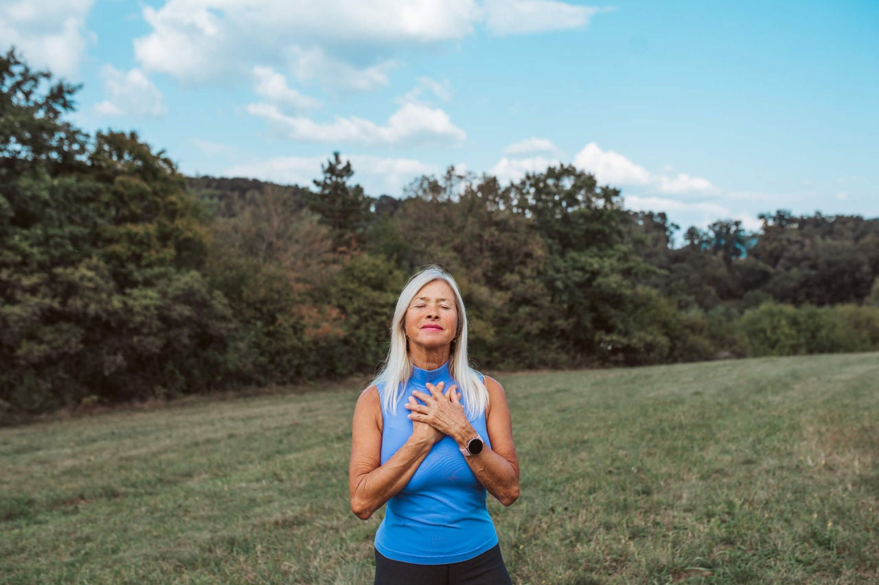Woman in a field holding her hands over her heart with her eyes closed.