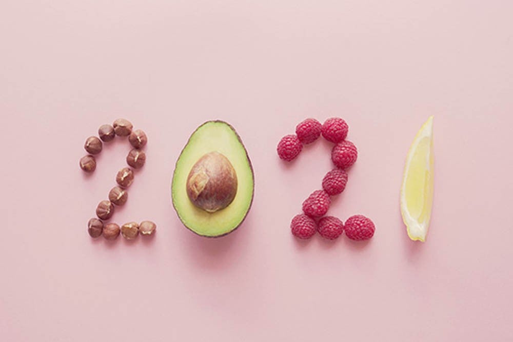 Los números "2021" formados con nueces y frutas, incluyendo medio aguacate y frambuesas, sobre un fondo rosa.